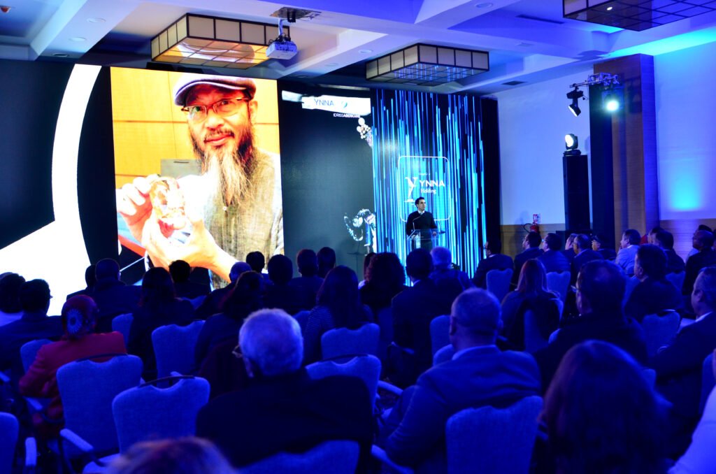 Ballet dancers in white tutus performing with raised arms on a dark stage with audience visible