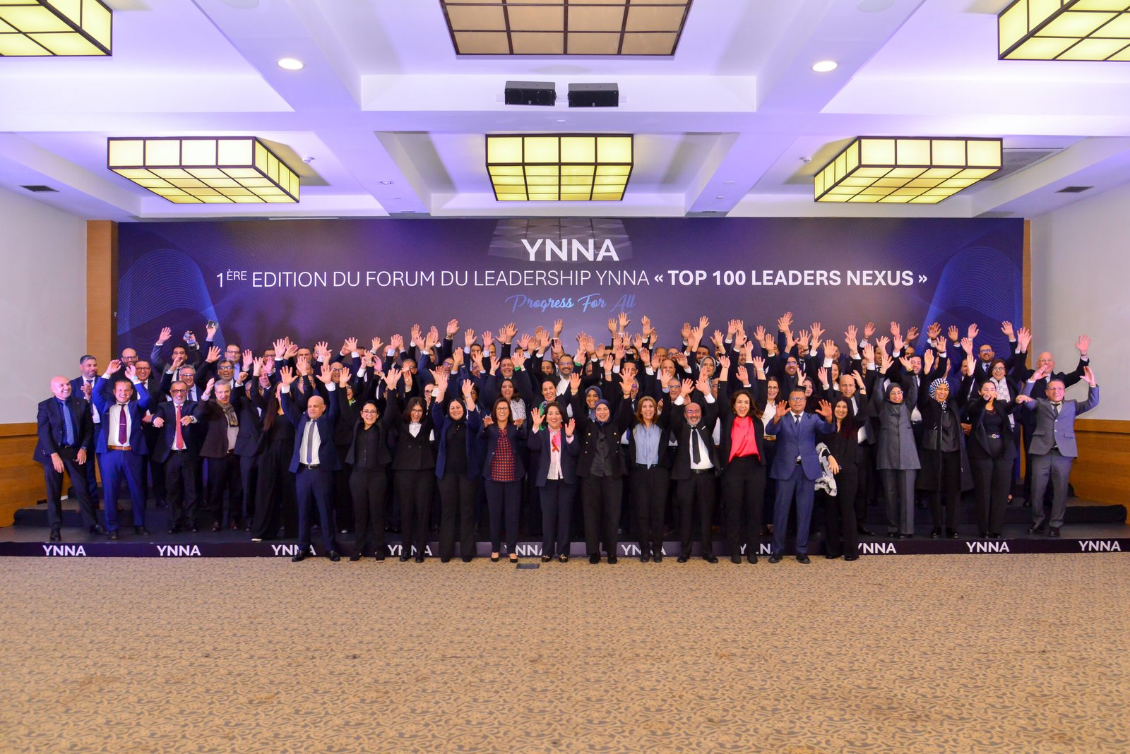 Ballet dancers in white tutus performing with raised arms on a dark stage with audience visible
